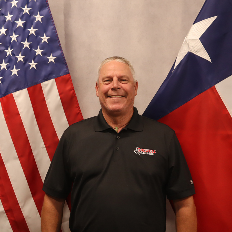 Colwell Electric team member smiling while standing between the American and Texas flags, showcasing company pride and professionalism.