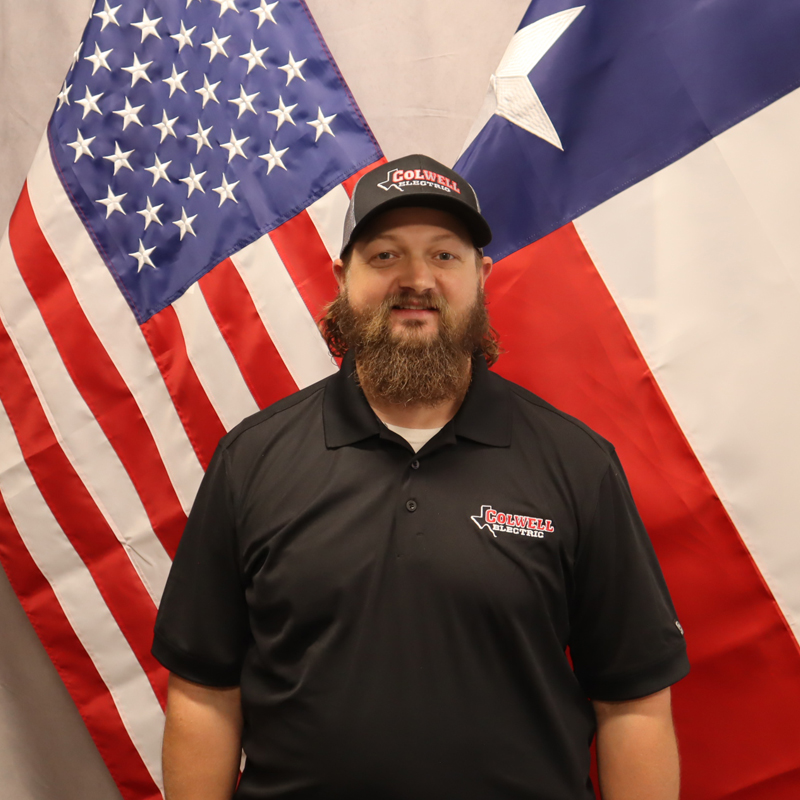 Colwell Electric team member in branded uniform and hat standing between the American and Texas flags, symbolizing company pride and leadership