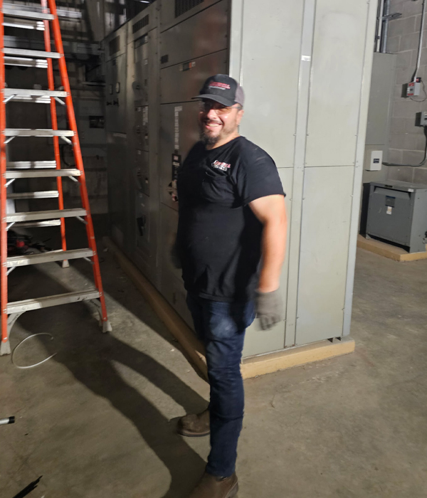 Electrician standing near industrial electrical panels and equipment, preparing for maintenance work inside a commercial facility.