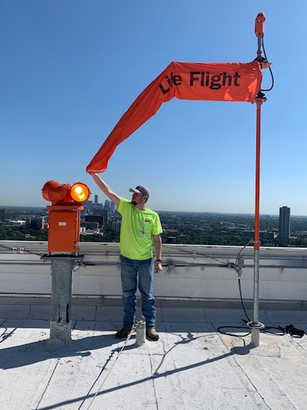 Electrician inspecting rooftop Life Flight helipad lighting and wind direction indicator system on a high-rise building.