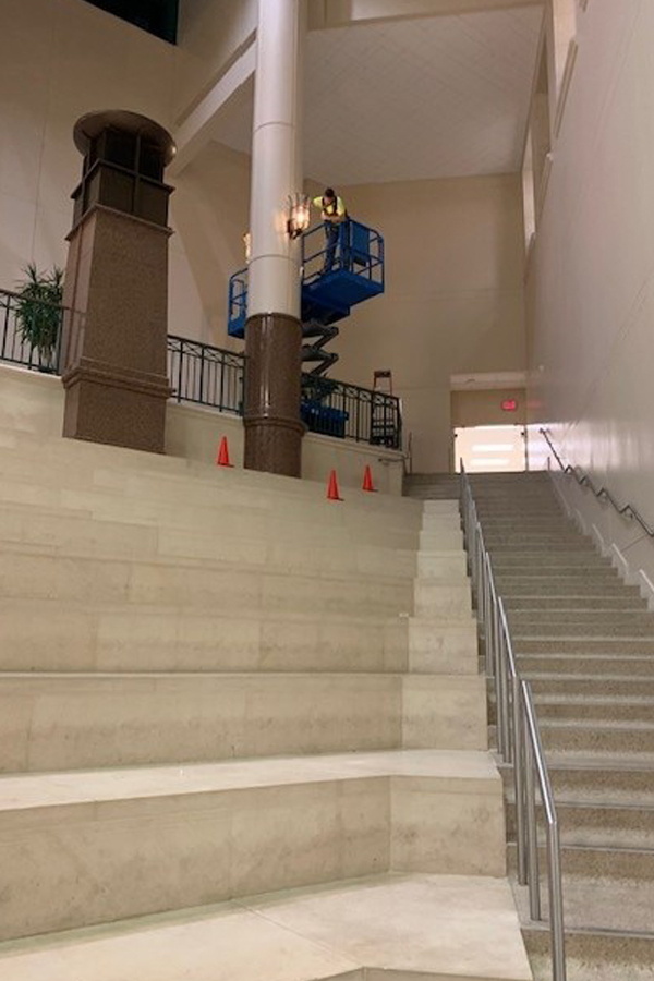 Electrician on a lift performing commercial lighting installation near tall columns inside a large building stairwell during electrical design-build construction.