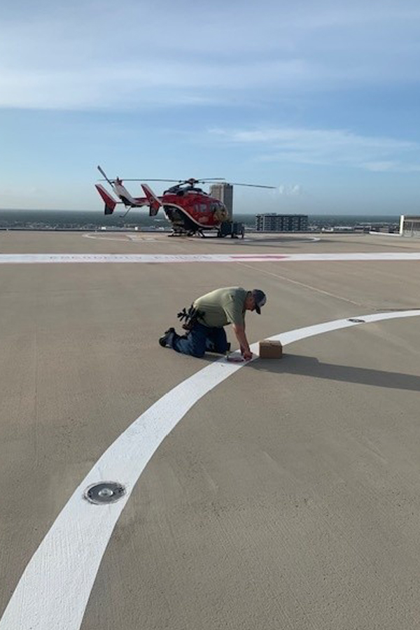Electrician performing maintenance on a hospital rooftop helipad lighting system with a medical helicopter in the background.