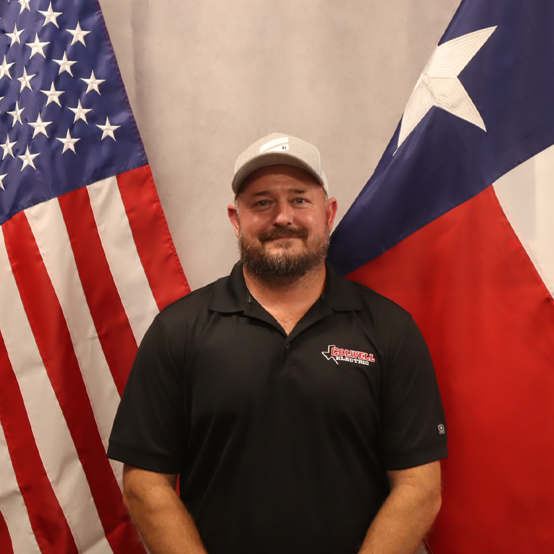 Team member from Colwell Electric standing between the American and Texas flags, representing the company’s pride and professionalism.