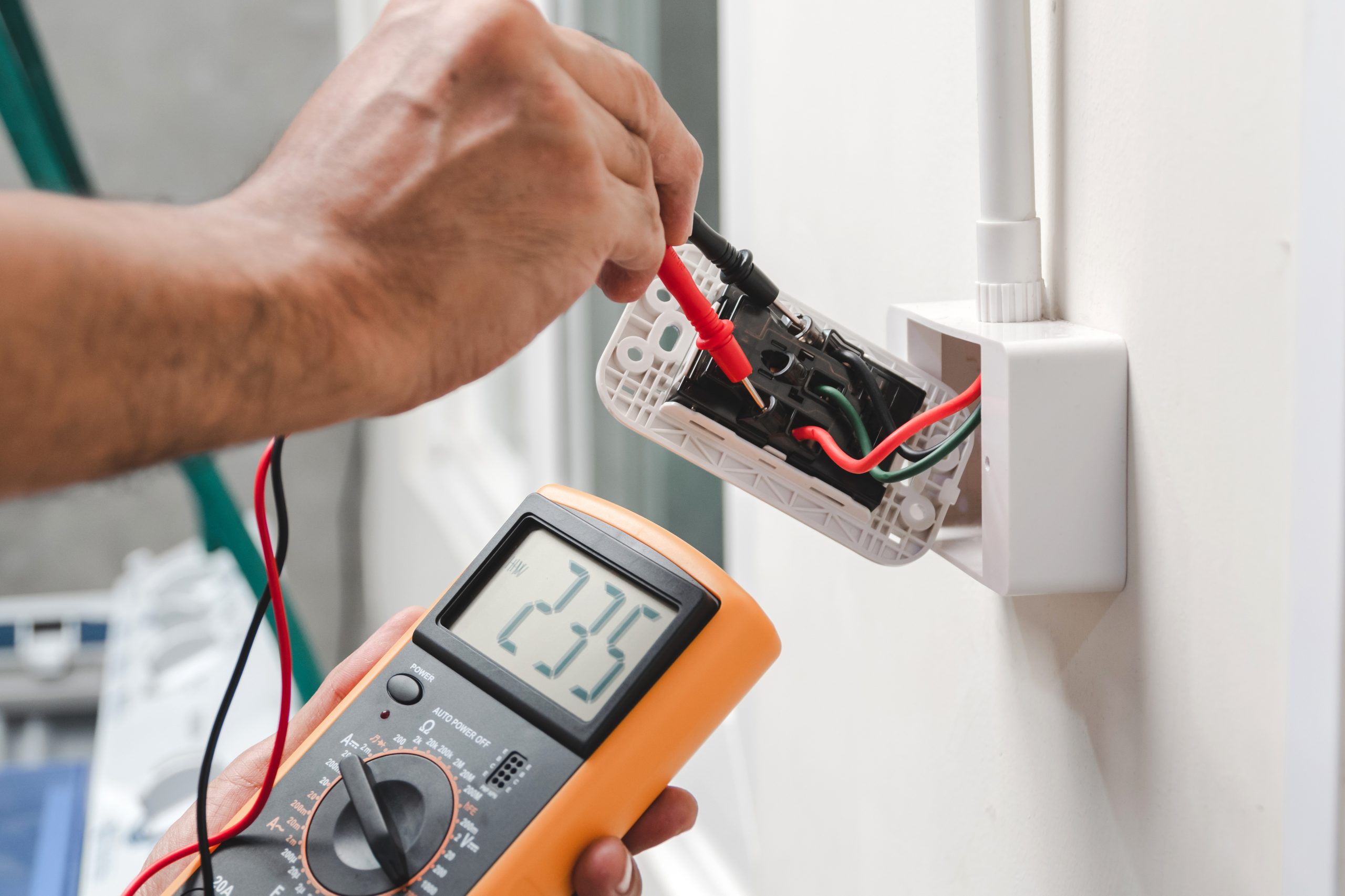Electrician performing a routine electrical inspection with a multimeter to check outlet safety and prevent costly repairs.