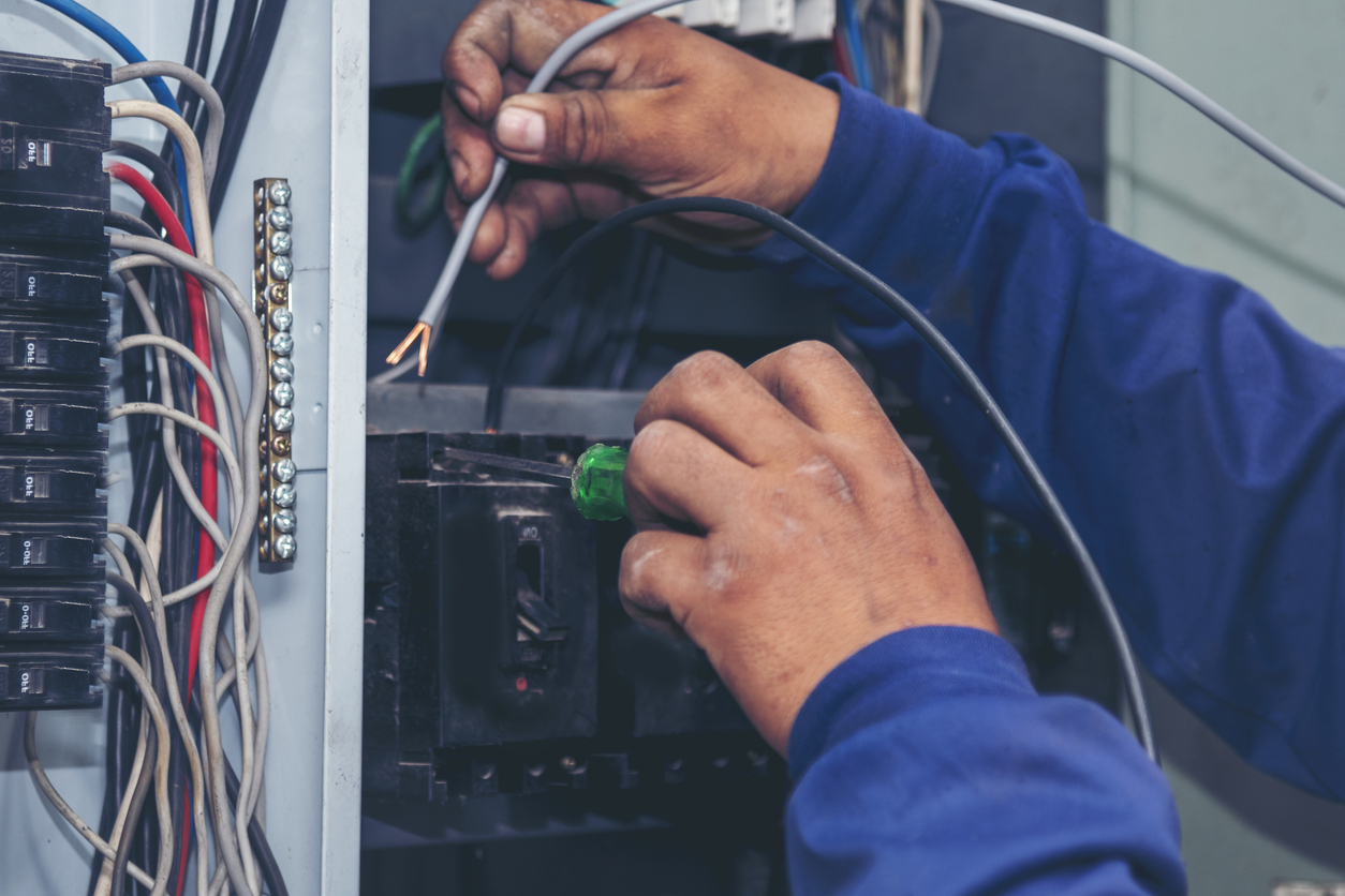 Electrician using a screwdriver to connect wires inside an electrical panel during maintenance or installation work.