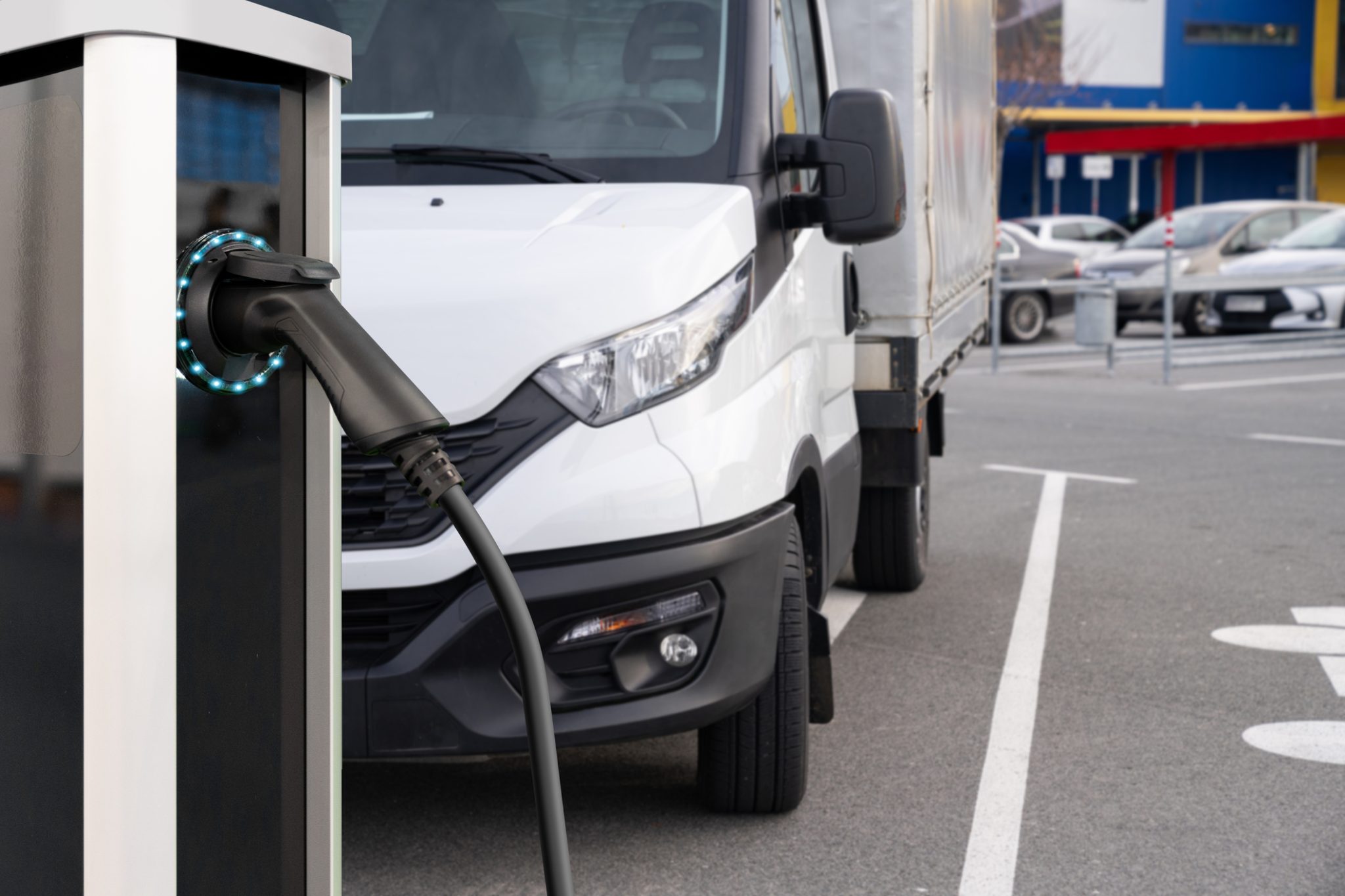 EV charging cable at a station in a parking lot, with a white delivery truck parked in the background.