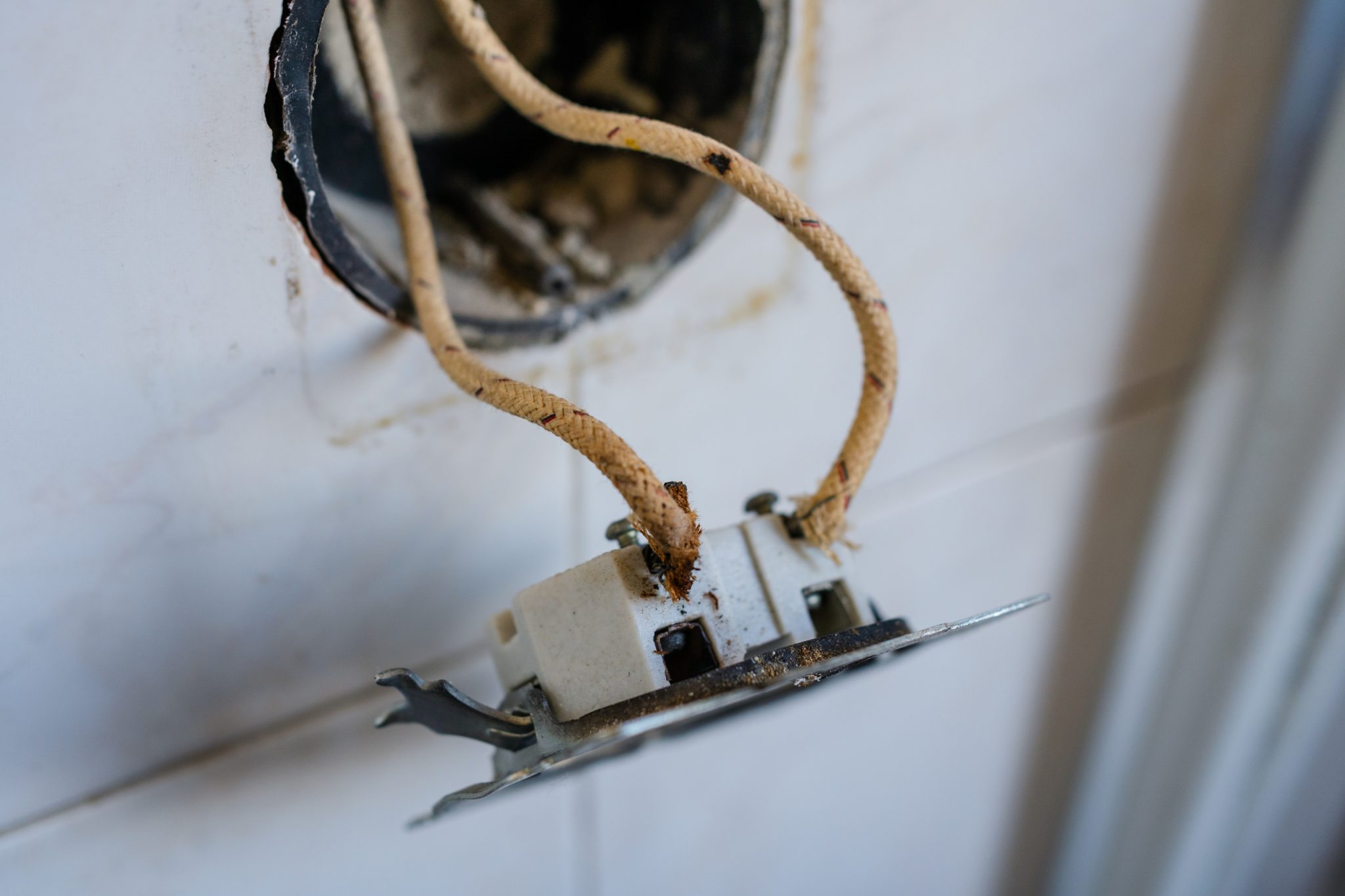 Frayed cloth-insulated wires hanging from an old ceramic outlet pulled out of a wall box in an older home.